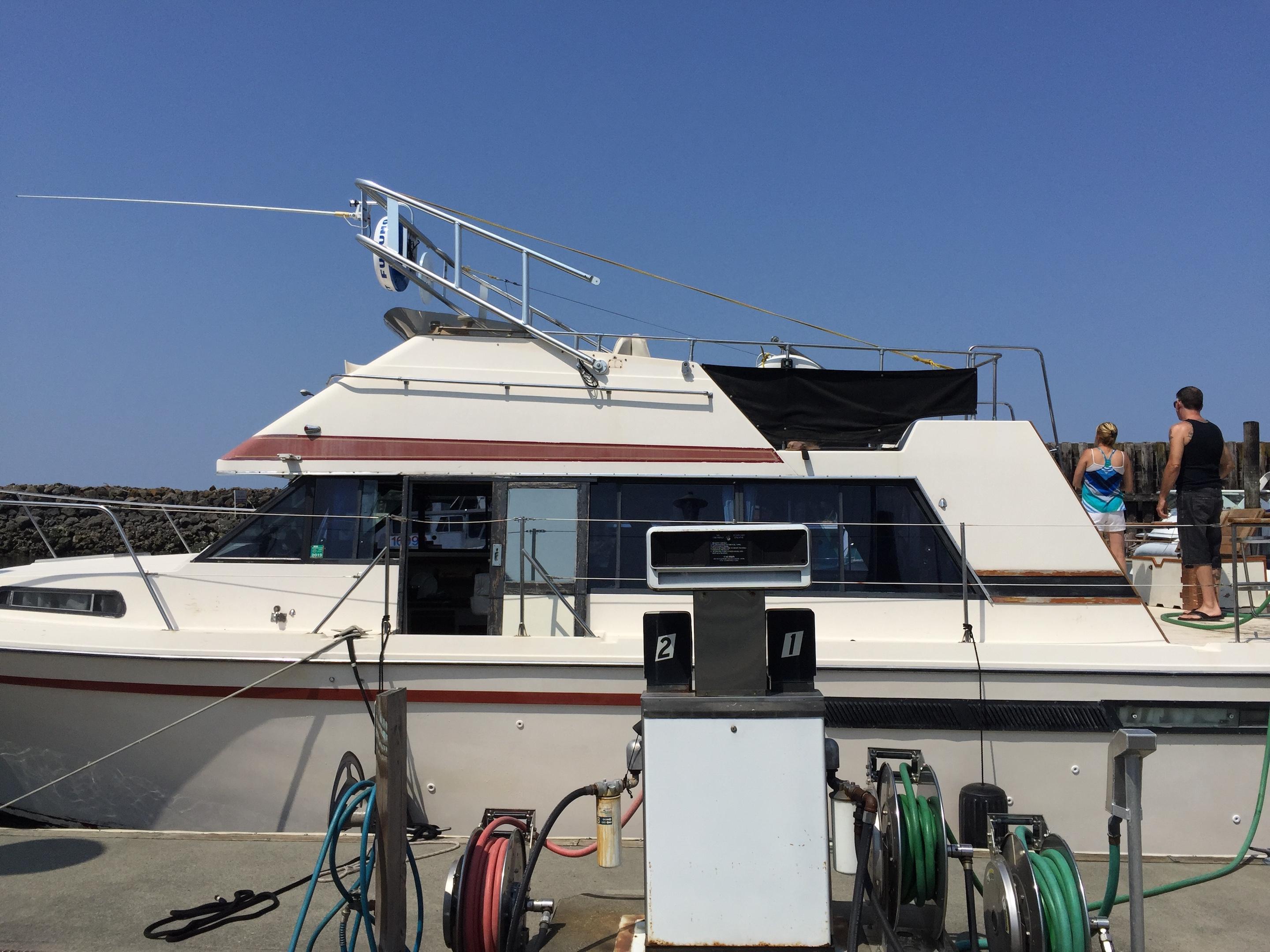 Bayliner boat docked with an installed Atlantic Towers arch and two people standing on the rear deck under a clear sky.