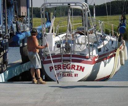 Sailboat named Peregrin from City Island, NY, docked with a man working near the Atlantic Towers Arch installed on the stern.