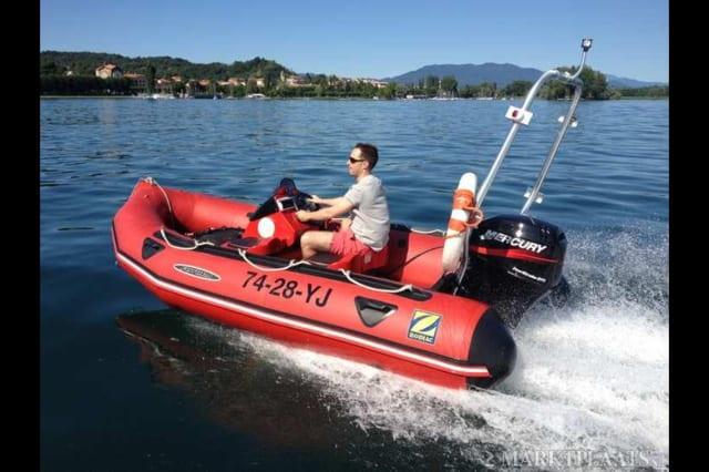 Man driving a Zodiac inflatable boat equipped with an Atlantic Towers Arch and Mercury outboard motor on calm water near a shoreline.