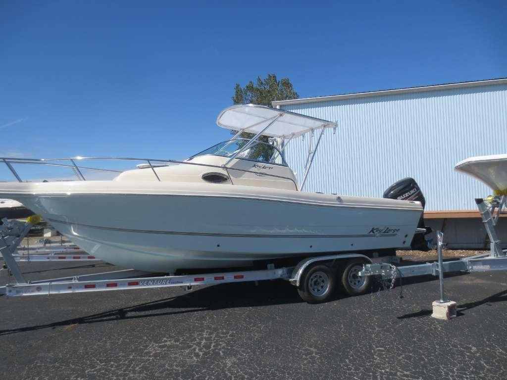 Key Largo boat with Atlantic Towers Top installed, sitting on a dual-axle trailer in a parking lot near a building.