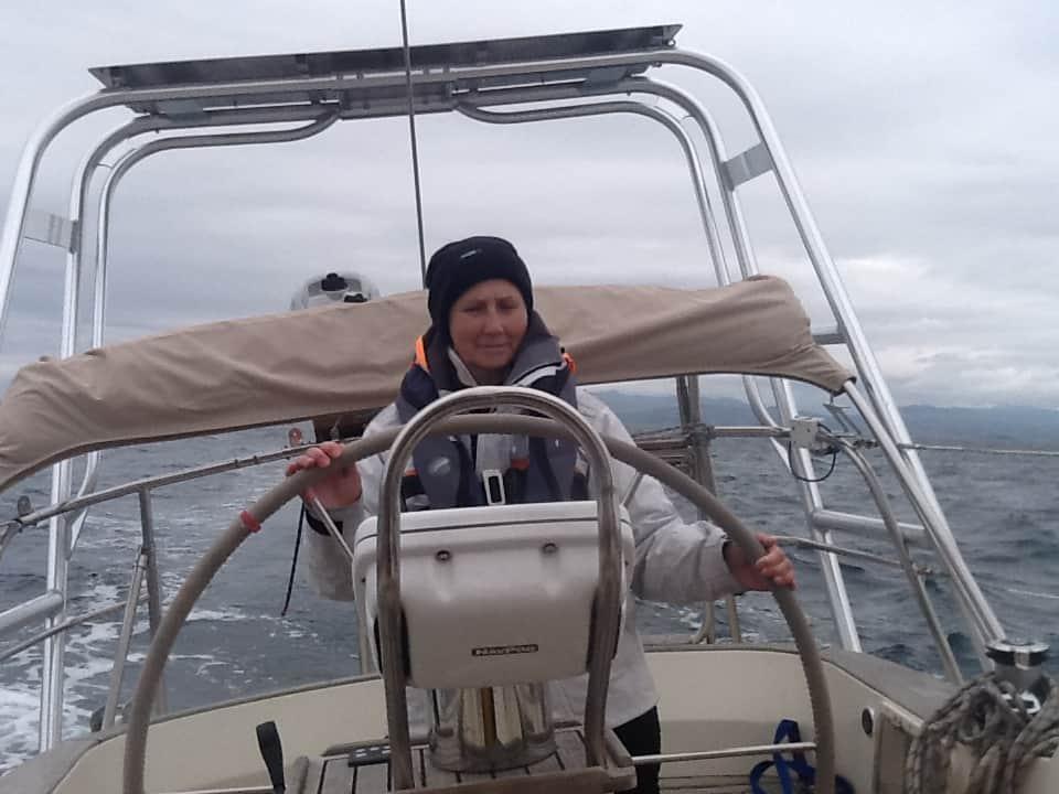 Person steering a boat at the helm with Bowman Atlantic Towers Arch overhead on a cloudy day at sea.