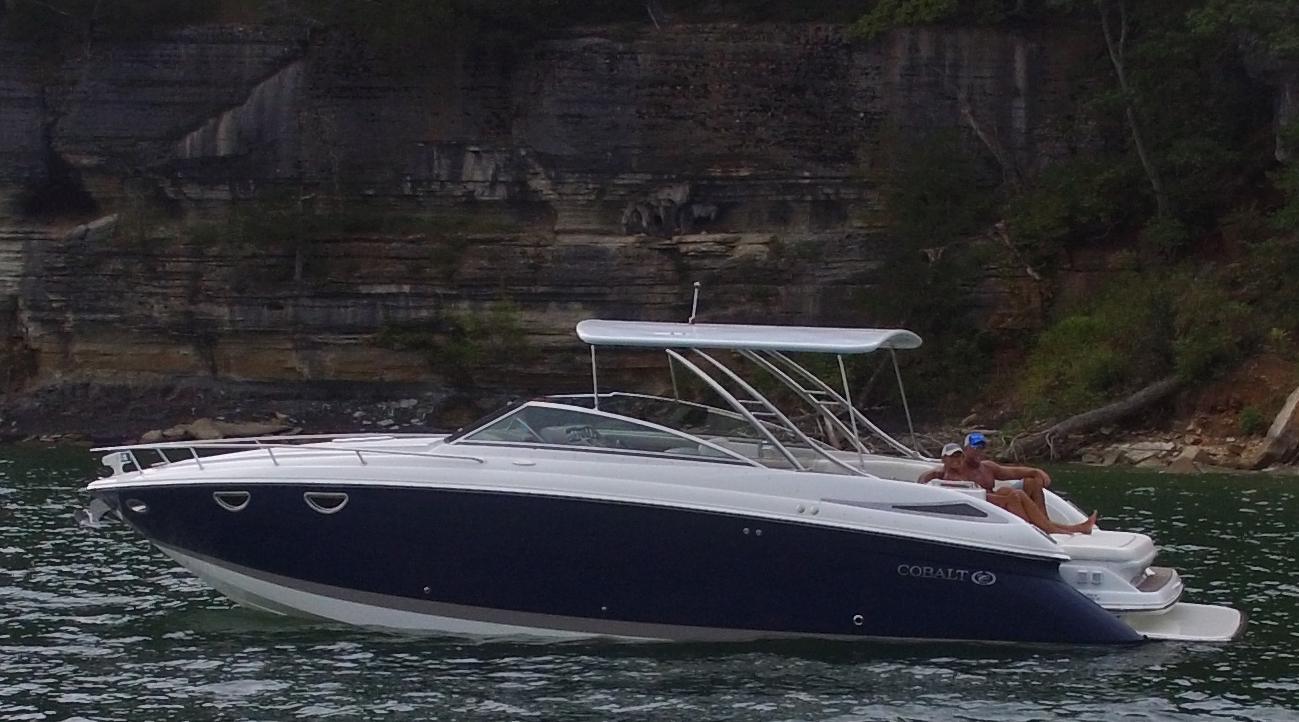 Cobalt boat with Atlantic Towers Top installed, anchored near a rocky shoreline with two people relaxing on deck.