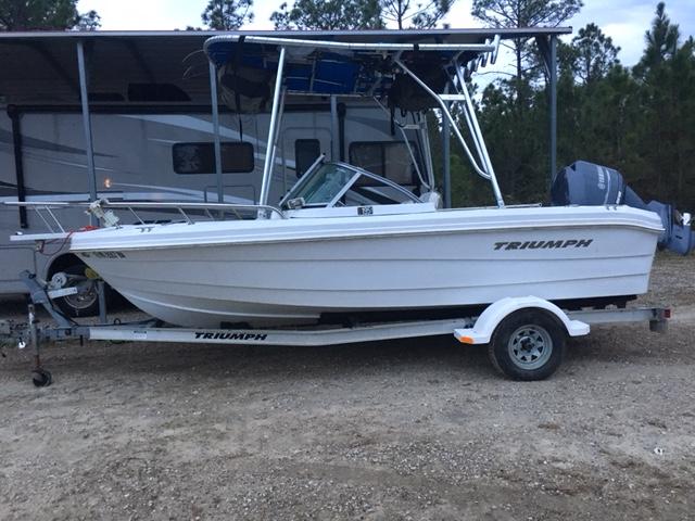 White Triumph boat on trailer with installed Atlantic Towers Top canopy, parked outdoors near a camper and trees.
