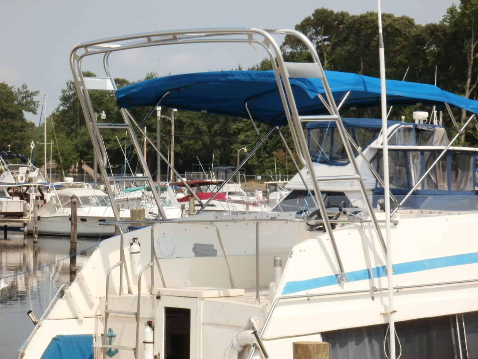 Atlantic Towers Arch installed on a Trojan 32 boat, with a blue canvas top, docked at a marina surrounded by various boats.