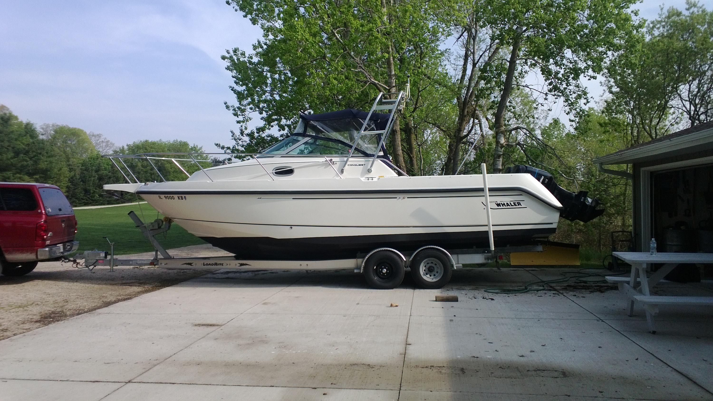 White boat on a trailer hitched to a red SUV parked on a concrete driveway, featuring an Atlantic Towers Arch installed on the cabin roof.