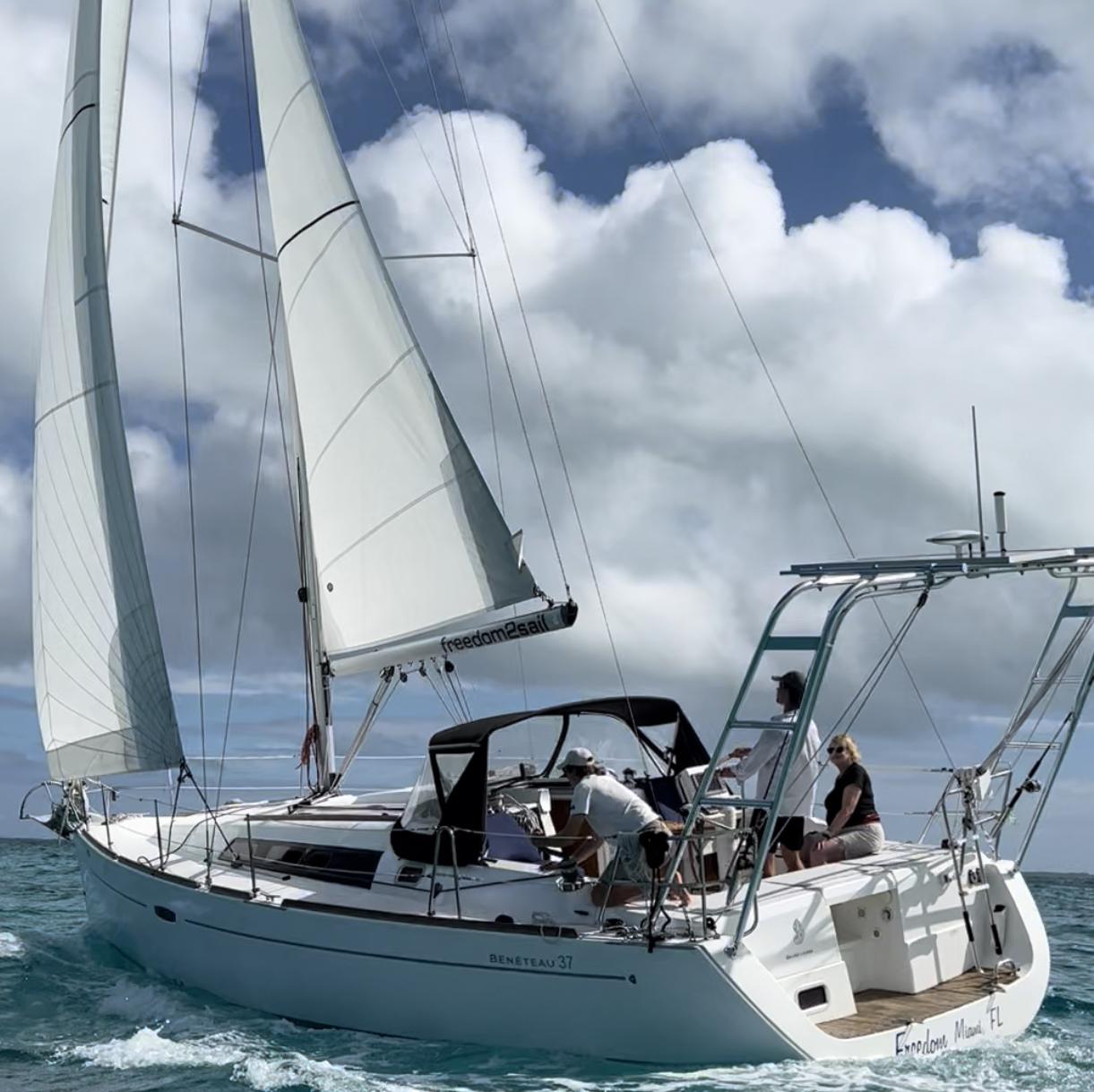 Sailing yacht with white sails and a cockpit covered by an Atlantic Towers Arch, with three people onboard under a partly cloudy sky.