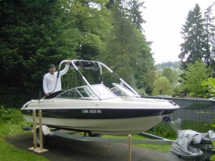 A person stands on a trailer beside a boat equipped with Atlantic Towers accessories amidst greenery.