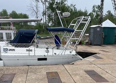 Atlantic Towers arch installed on the stern of a white Beneteau sailboat docked near a wooden pier and trees.