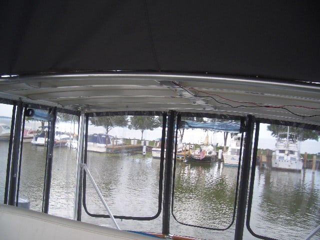 Interior view of a boat with a black canopy, showing the marina and moored boats in calm waters.