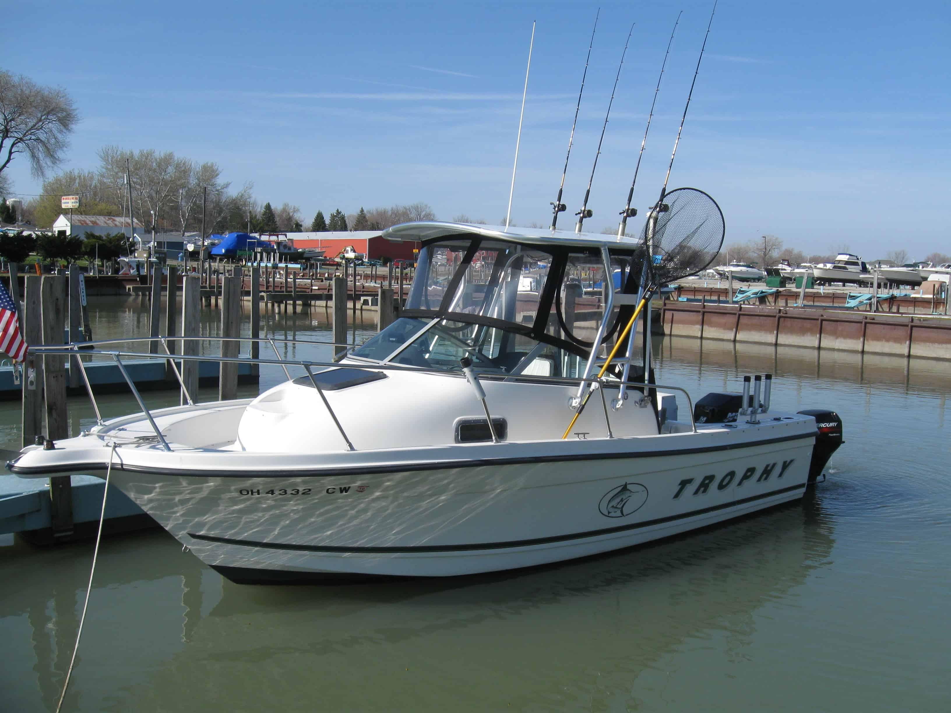 White fishing boat docked at marina with clear sky, fishing poles, and net visible on board.