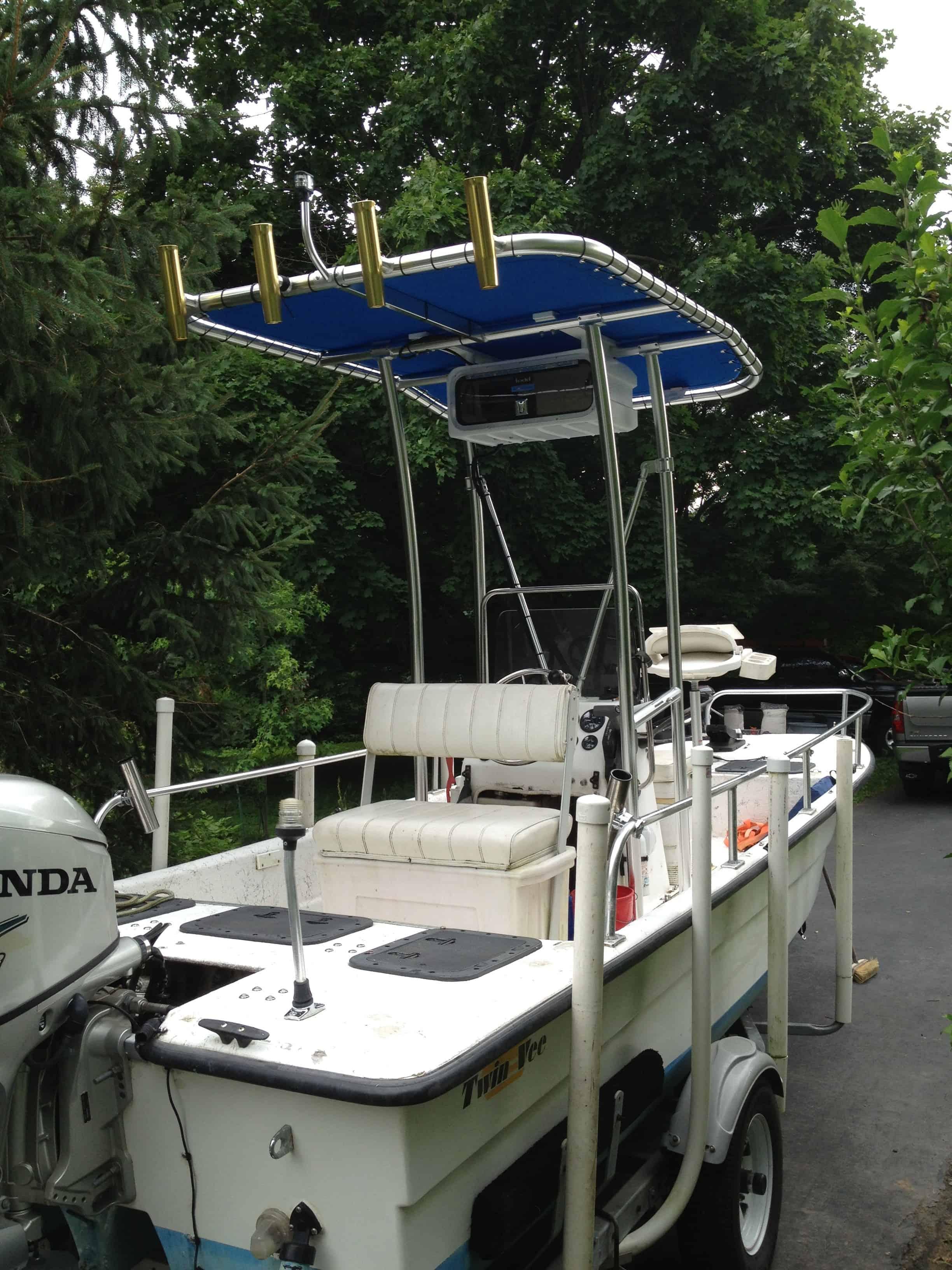 Small fishing boat on a trailer with a blue T-top canopy, white cushioned bench seat, and mounted rod holders.