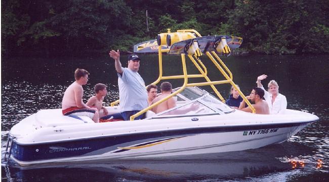 Alt text: Atlantic Towers boat with eight people enjoying a day on the water, featuring a wakeboard rack and scenic background.