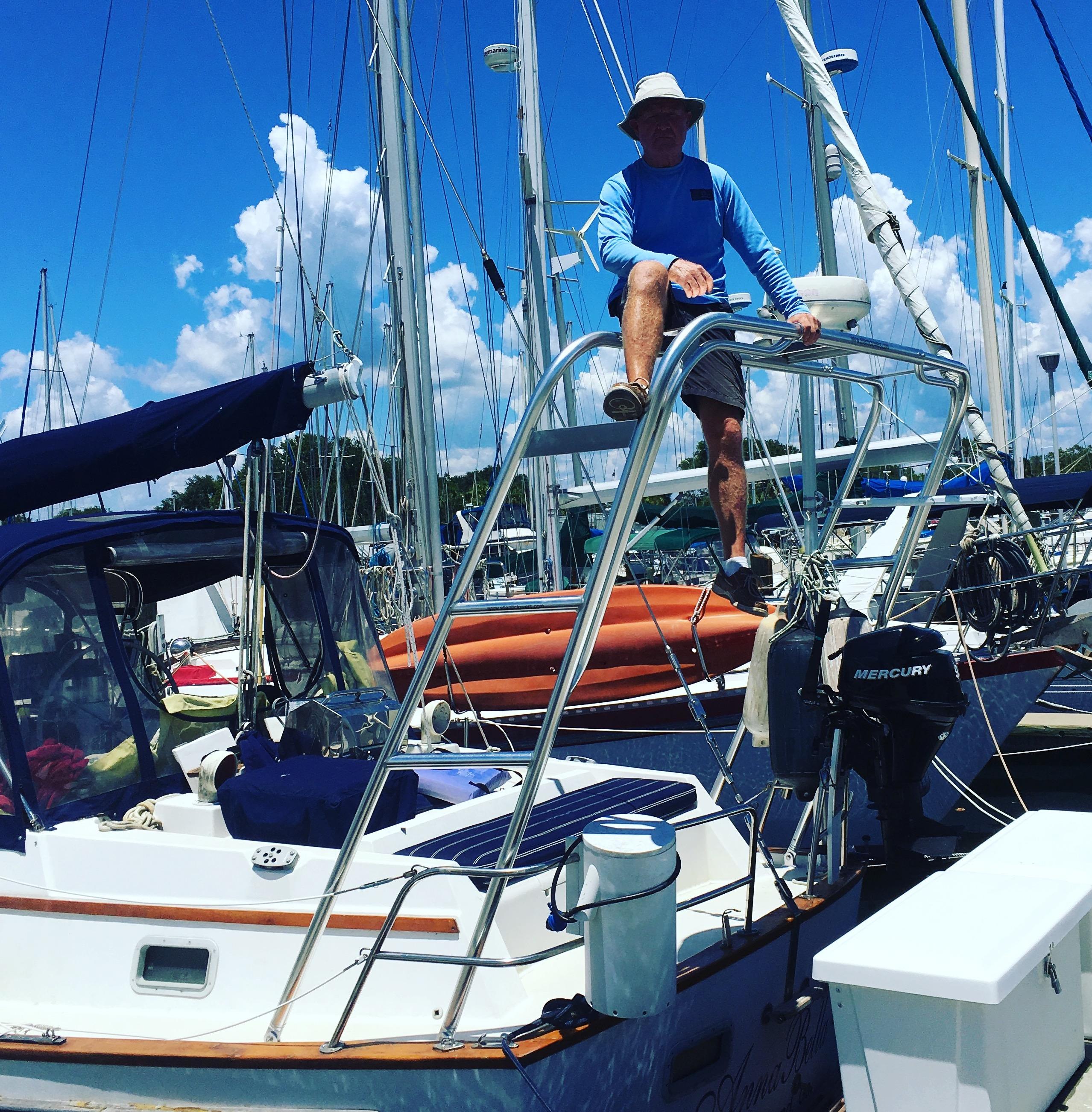 Man sitting on stainless steel Atlantic Towers arch installed on the stern of a Pearson sailboat in a marina on a sunny day.
