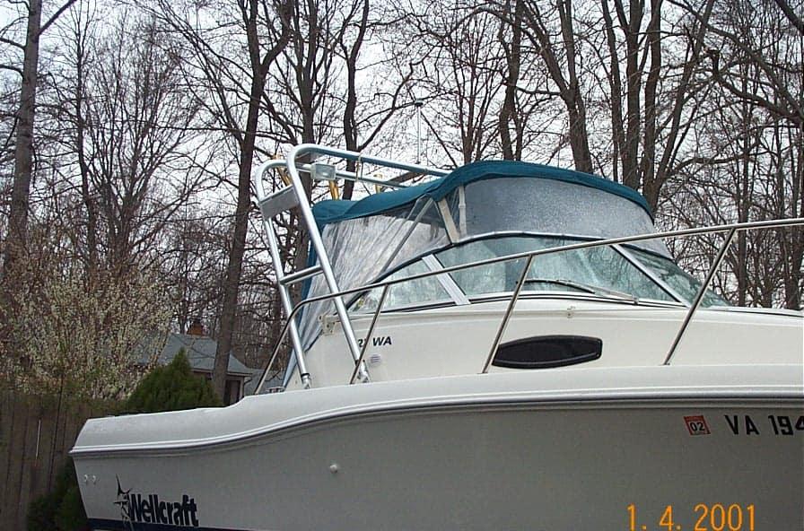 Atlantic Towers boat with a blue bimini top, parked among trees in a residential area.