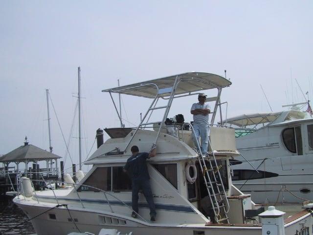 Two men working on a Chris Craft 36 Commander boat with an Atlantic Towers Top at a marina.