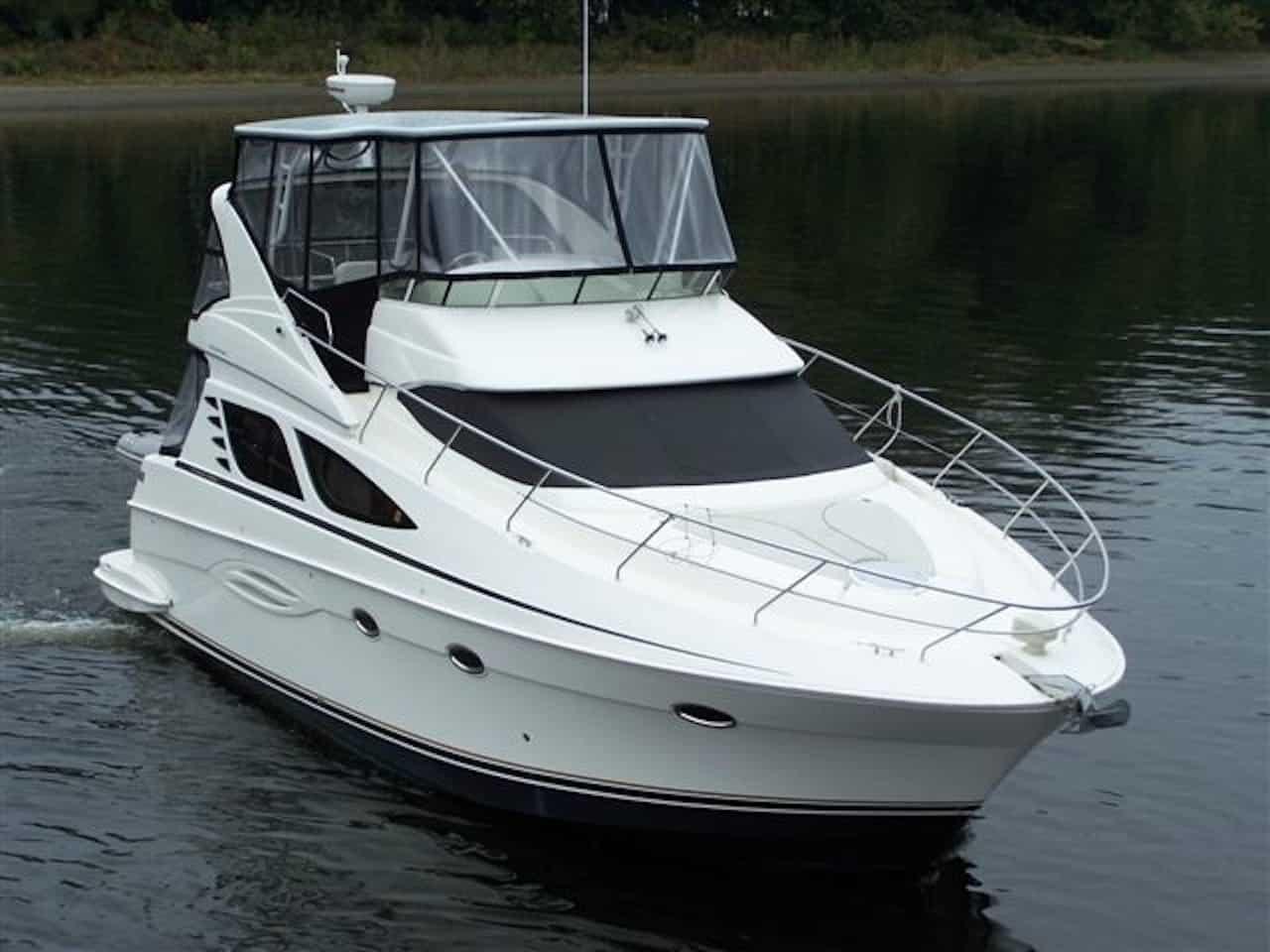 White motor yacht cruising on calm water with tinted windows and black canvas covering the upper deck and windshield.