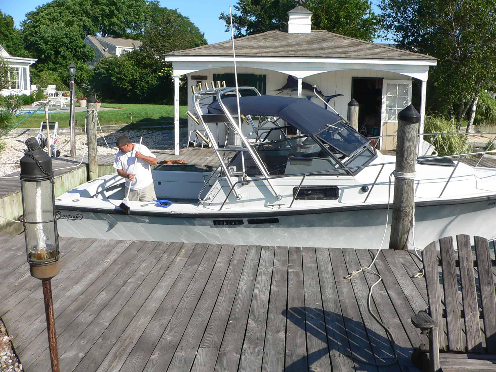 Man cleaning a white Rampage 28 Sportsman boat docked beside a wooden pier with Atlantic Towers Arch installed.