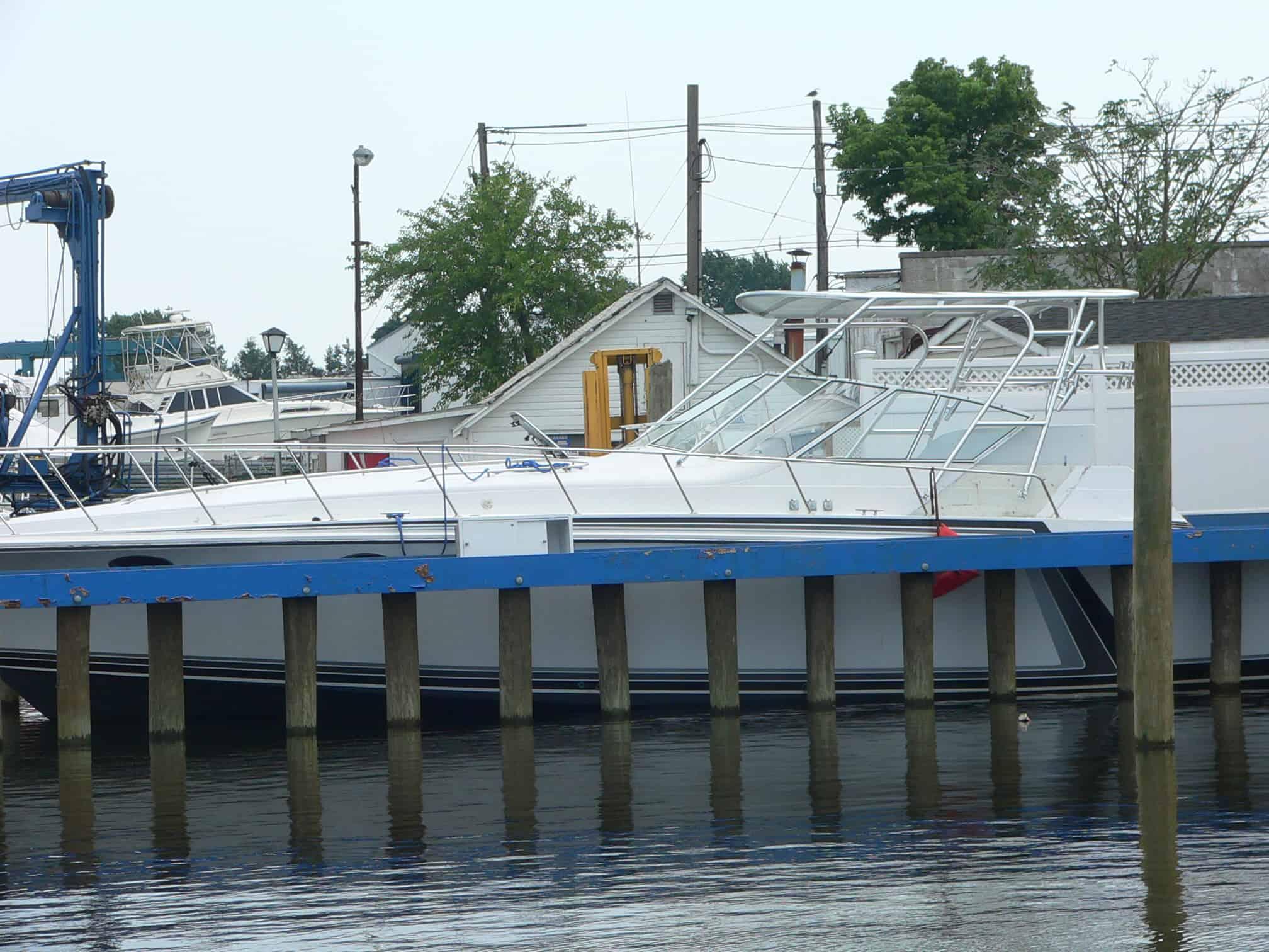 Trojan 13 Meter Express boat docked with an installed Atlantic Towers Top on the canopy frame near a small marina building.