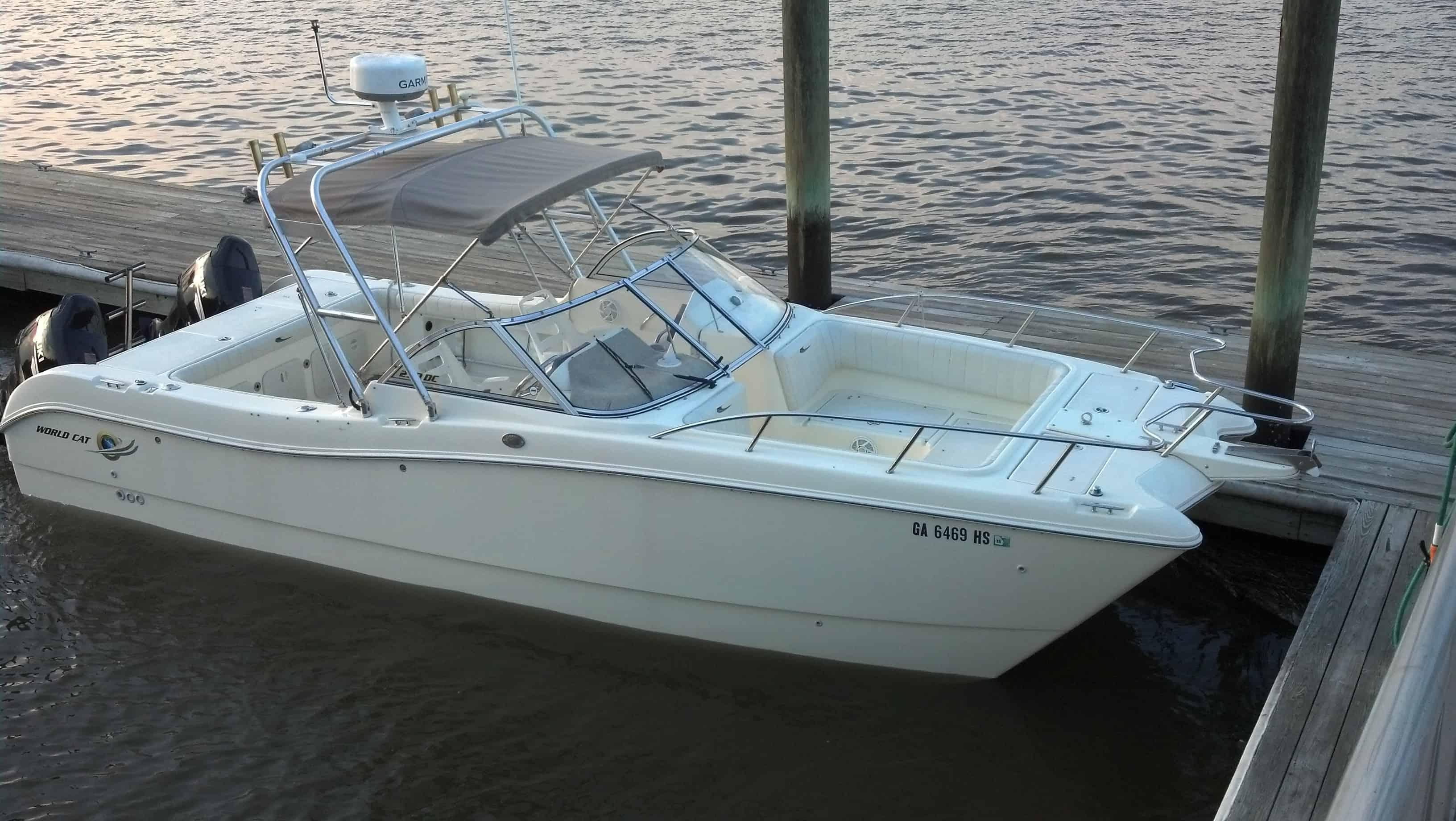 White motorboat with two outboard engines docked at a wooden pier in calm water during early evening.
