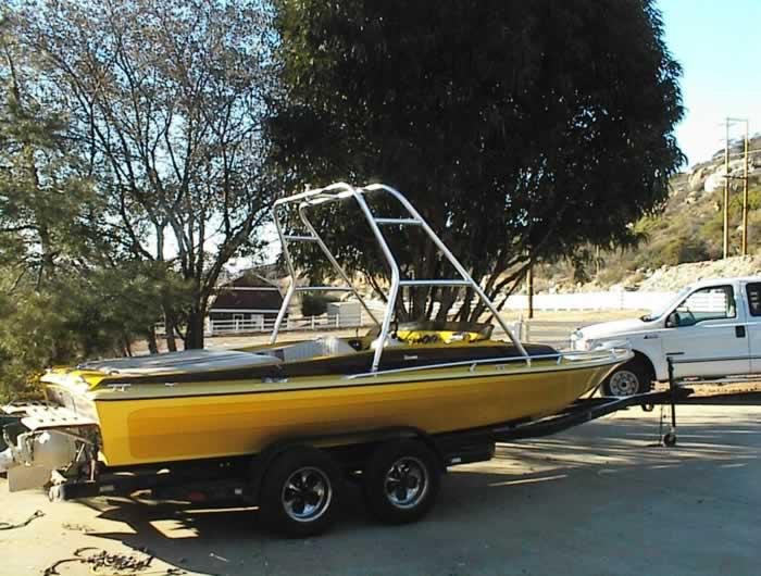 Alt text: Atlantic Towers Air Tower installed on a yellow boat parked on a trailer amidst trees and a truck in the background.
