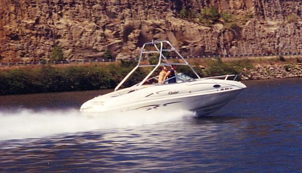 Rinker boat equipped with Atlantic Towers Air Tower speeding on a lake near rocky cliffs with two people onboard.