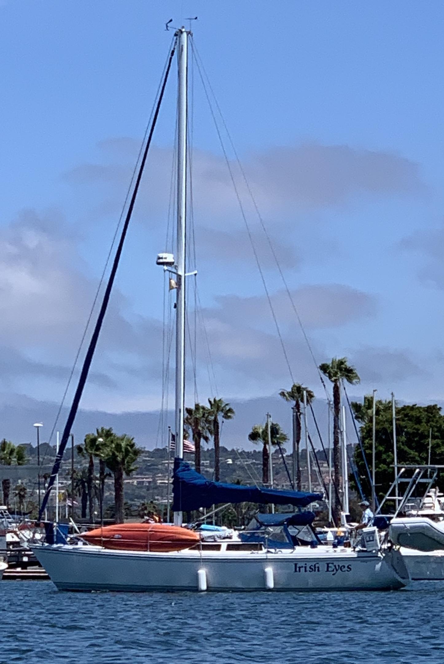 Sailboat named Irish Eyes docked with Atlantic Towers arch and folded orange kayak on deck under clear sky.