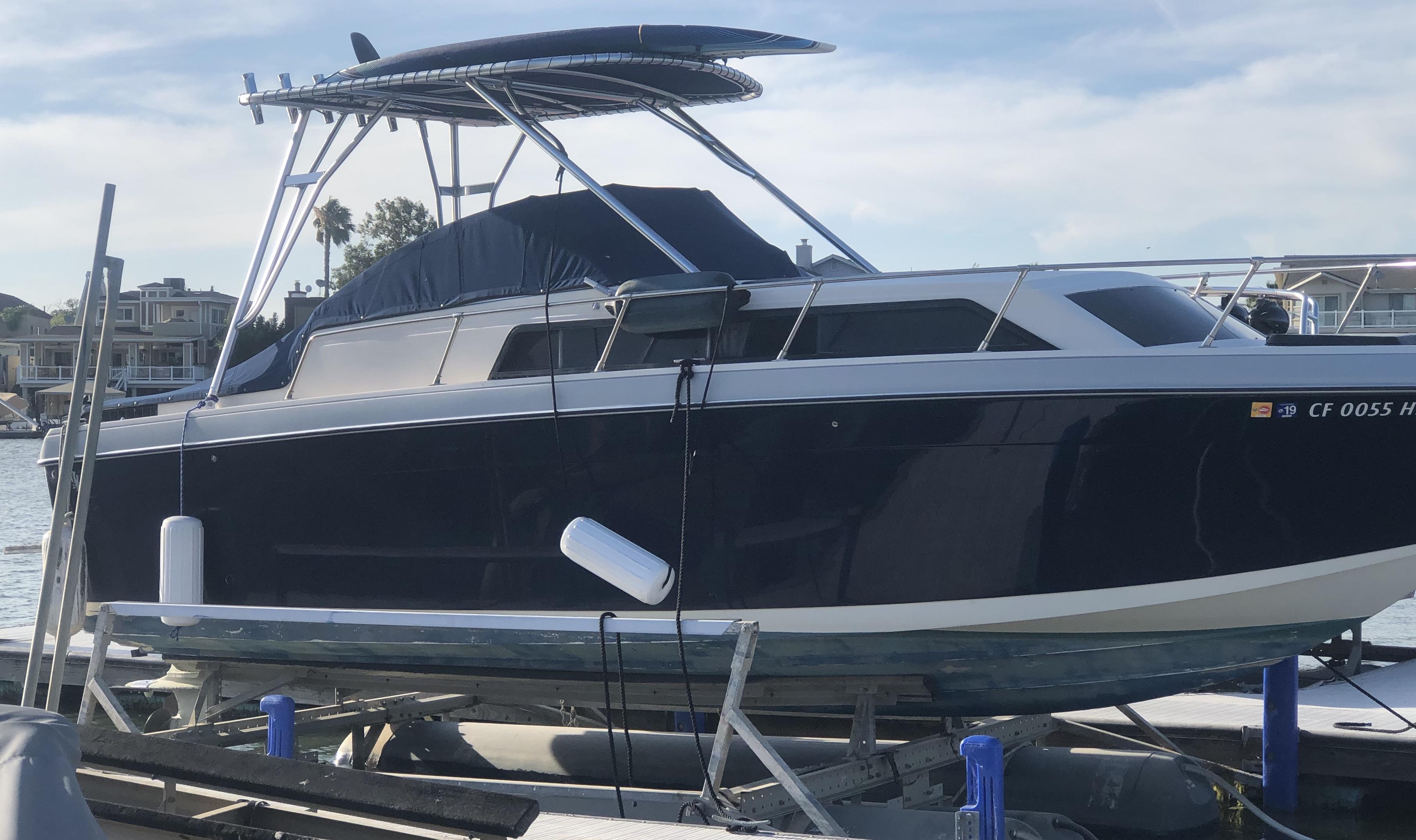 Side view of a Formula boat with a dark blue hull and a black canvas cover, equipped with an Atlantic Towers Top frame and canopy.