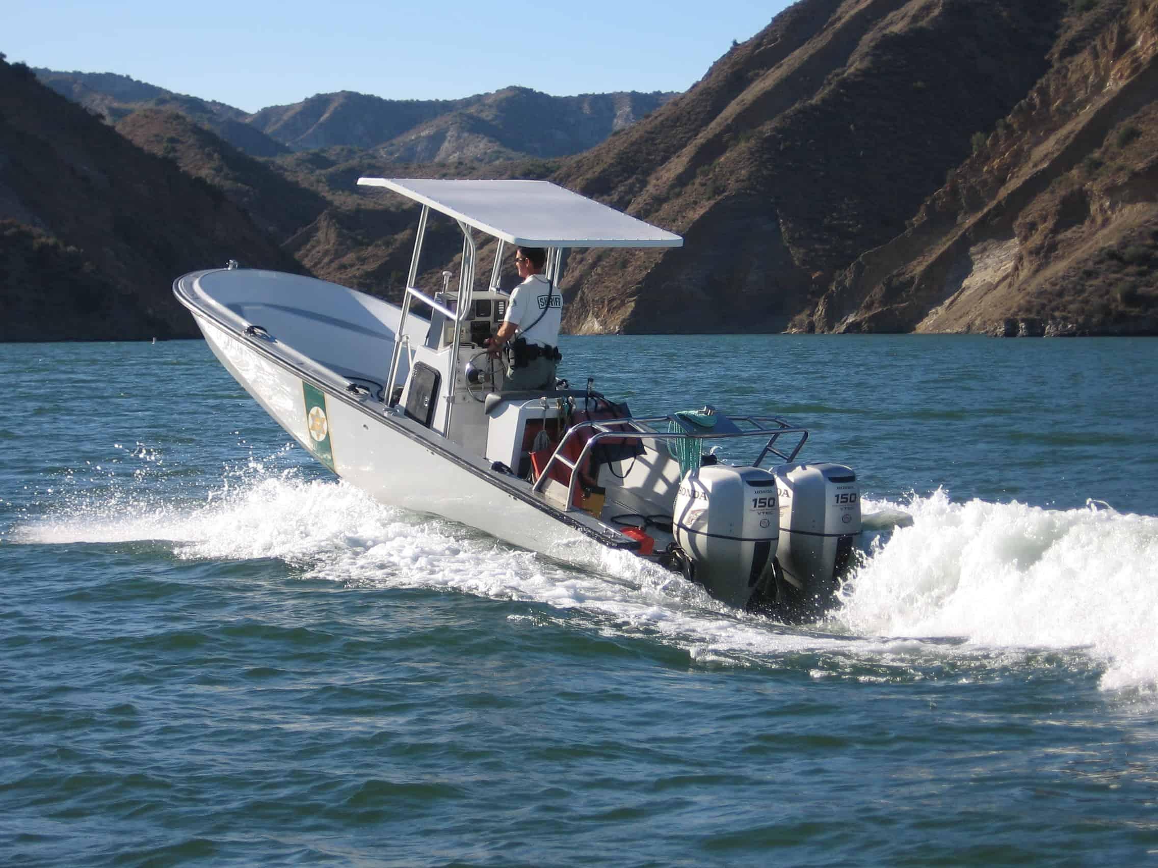 Boston Whaler Guardian boat with Atlantic Towers T-Top driven by a man on a body of water near rugged brown hills.
