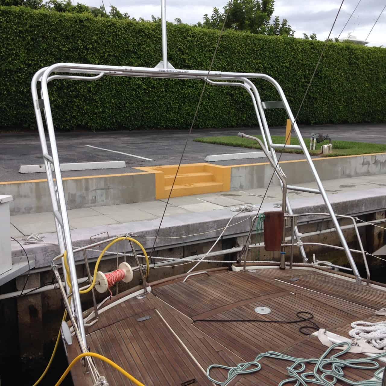 Atlantic Towers boat arch mounted on wooden deck of a docked boat with yellow and blue ropes nearby and green hedge in background.