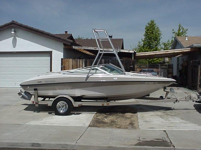 White and beige Blue Water Boats model with Atlantic Towers Air Tower mounted, parked on trailer in residential driveway.