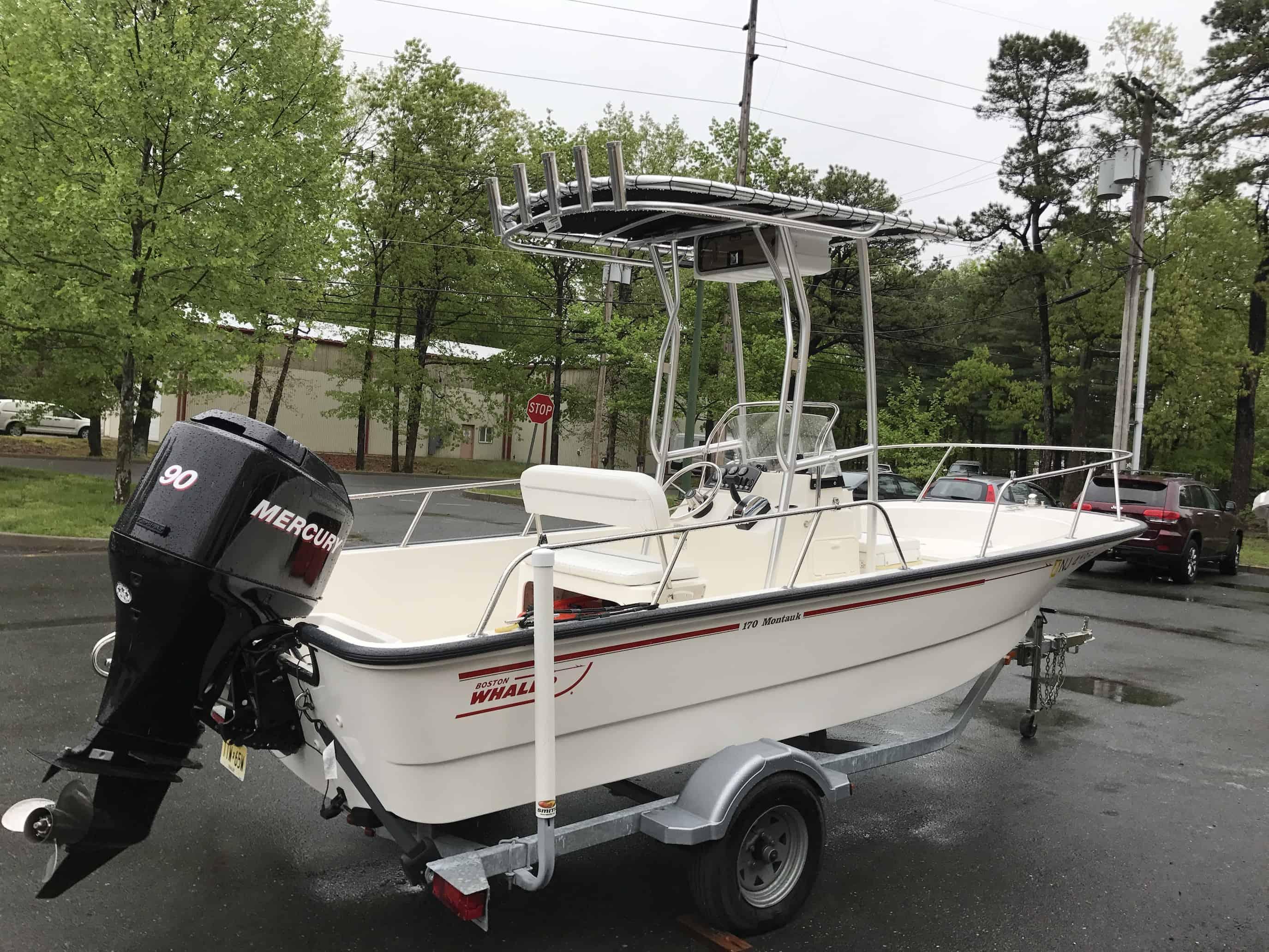 Boston Whaler boat with black Mercury outboard engine and Atlantic Towers T-Top on a trailer parked in a wet parking lot.