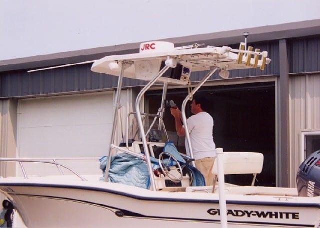 Grady White boat with installed Atlantic Towers T-Top showing man working on equipment beneath it near a garage.