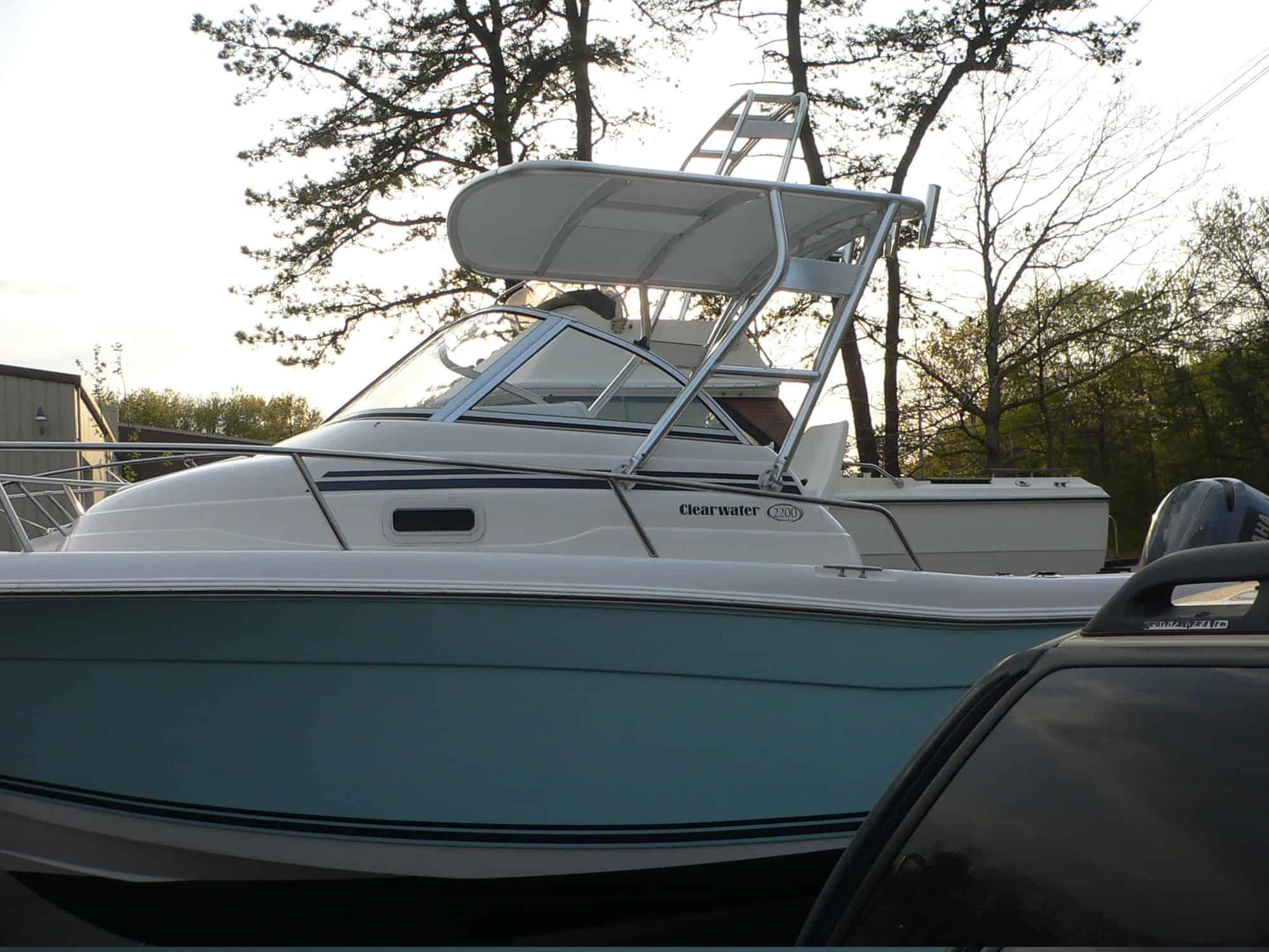 Atlantic Towers Top installed on a Clearwater Boats 2200 Walkaround with a white and light blue hull docked near trees.