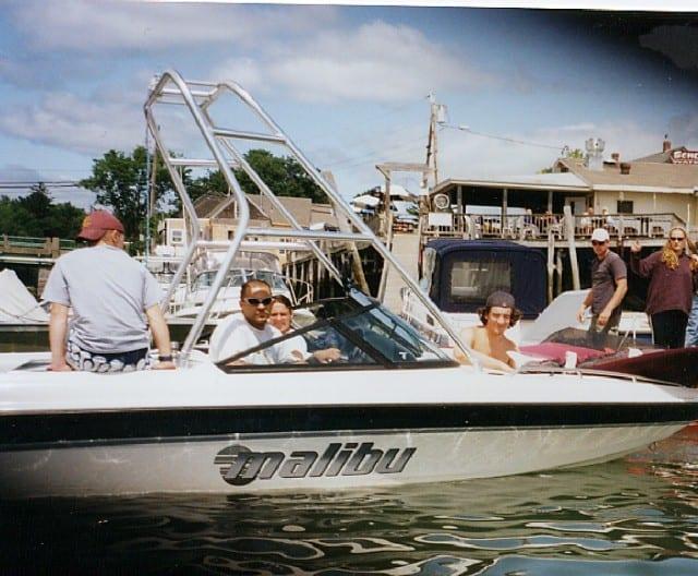 Malibu Sunsetter LX boat with Atlantic Towers Air Tower installed, carrying five people on calm water near a dock.