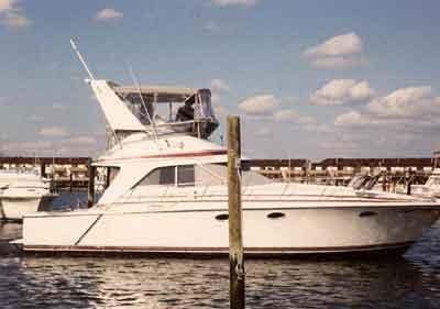 Side view of a Trojan 10.8 Meter Sedan boat with Atlantic Towers Arch installed, docked at a marina under blue sky.