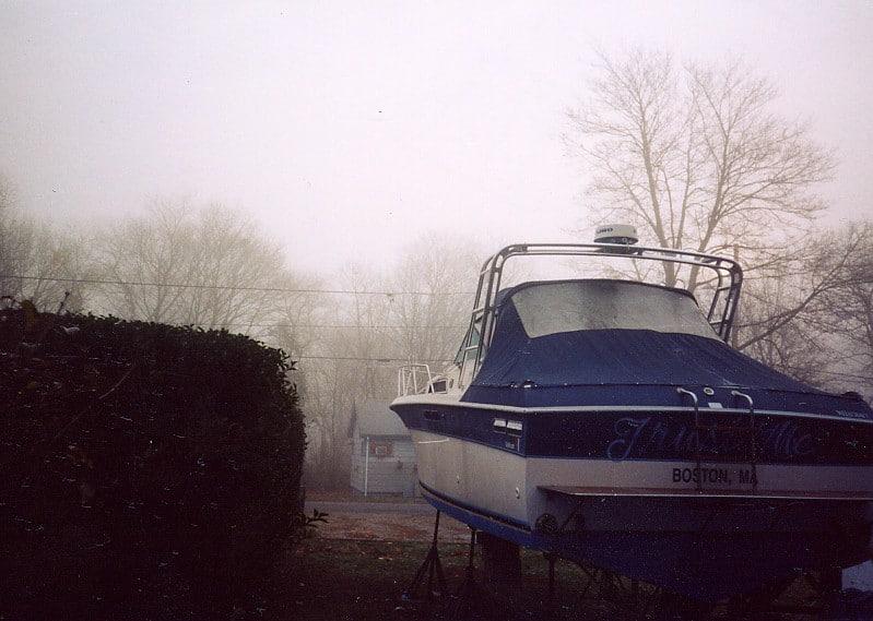 Wellcraft 2900 Express Cruiser with Atlantic Towers arch on dry land by trees and a hedge in foggy weather.
