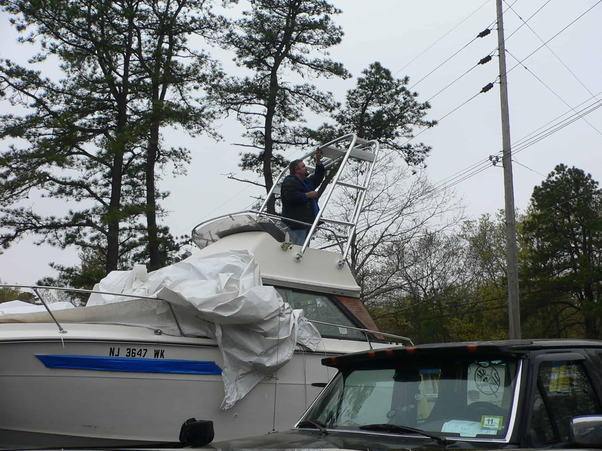 Man working on Atlantic Towers Arch installed on Sea Ray 24SRV Flybridge boat in an outdoor setting with trees and vehicles nearby.