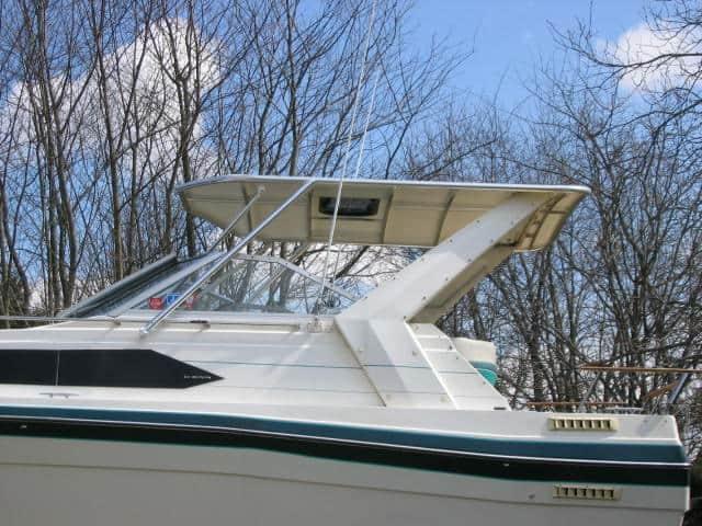 Side view of a Bayliner 2850 Contessa Sunbridge boat with an installed Atlantic Towers Top against a background of leafless trees.