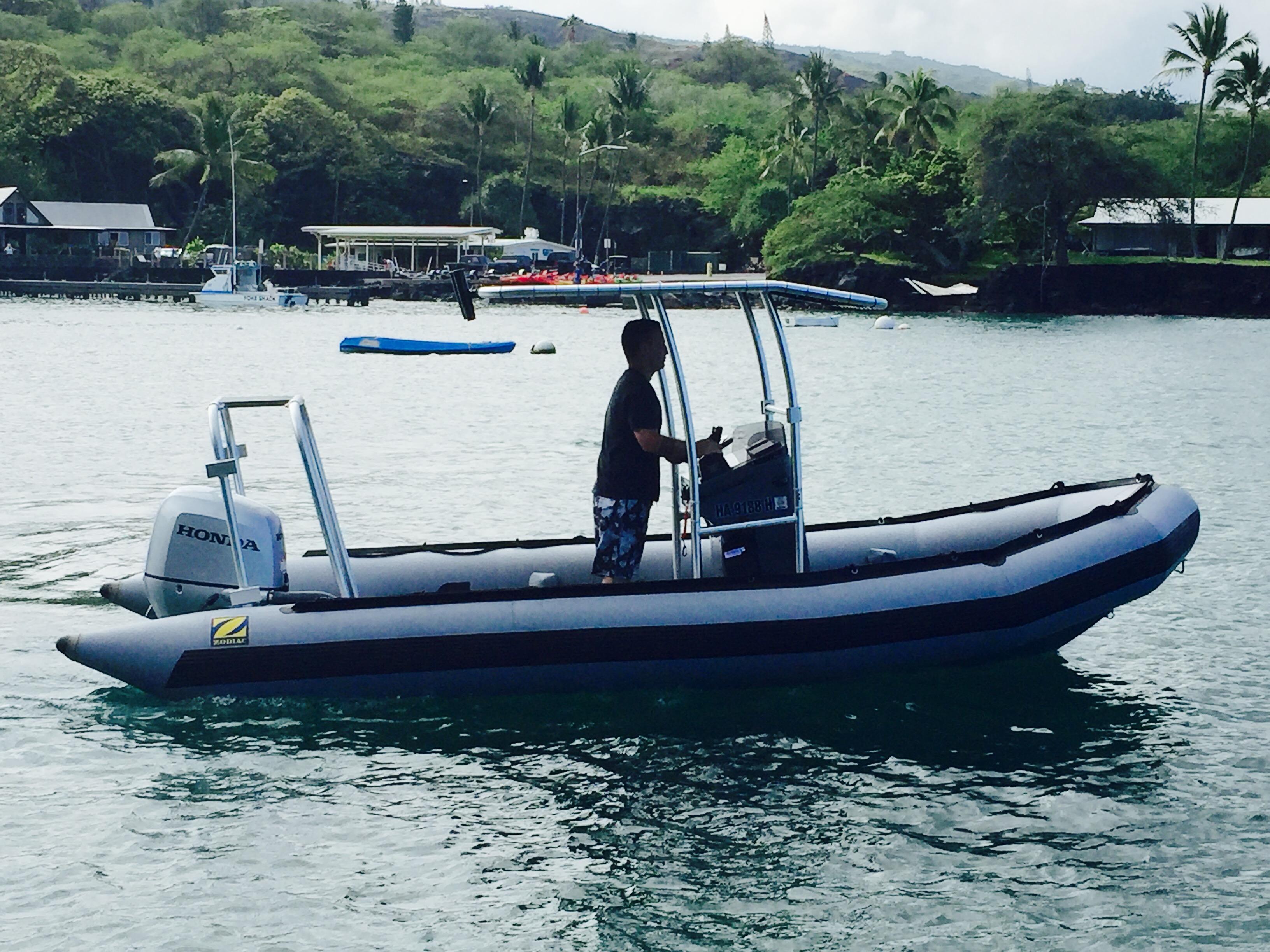 Zodiac boat with a man driving, featuring an installed Atlantic Towers arch on calm waters near a green shoreline.