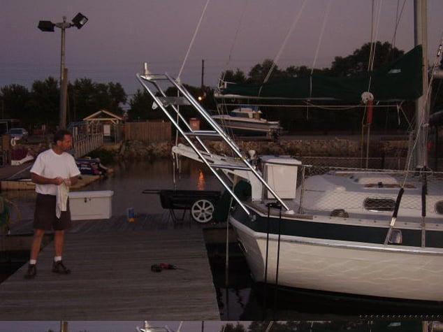 Atlantic Towers arch mounted on the back of a docked sailboat near a man standing on the wooden pier at dusk.