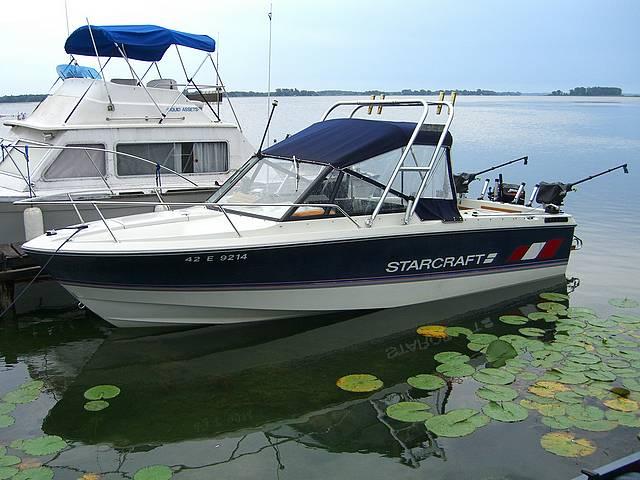 Starcraft 221 Offshore boat with Atlantic Towers Arch docked on a calm lake near lily pads and other boats.