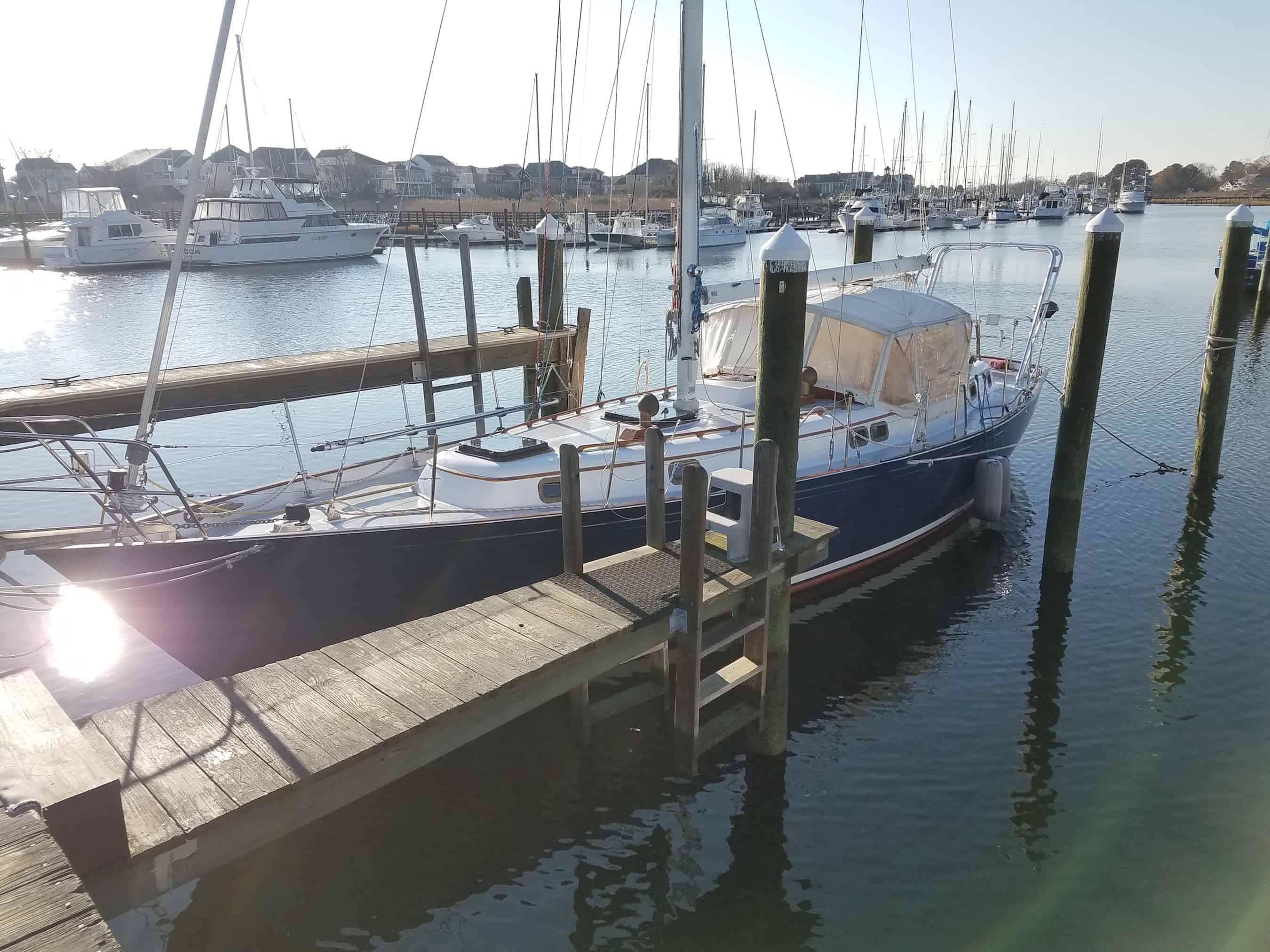 Sailboat equipped with Atlantic Towers Arch docked at a marina with wooden piers and other boats in background.
