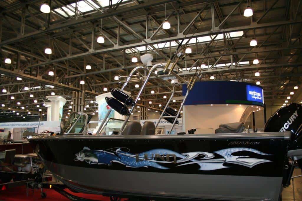Black and gray Lund 2150 La Baron boat with Atlantic Towers arch and fishing rods in an indoor exhibition hall.