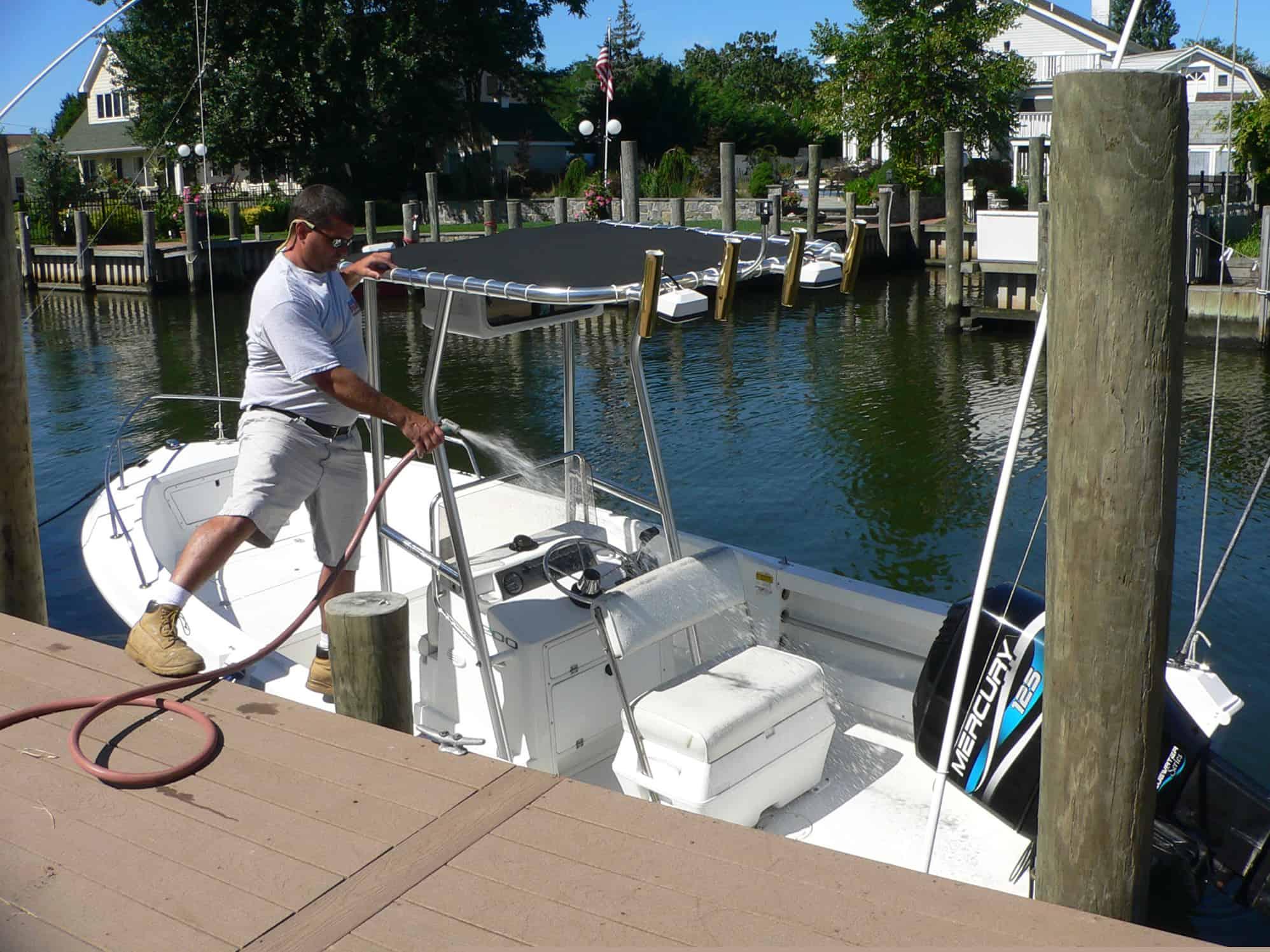 Man cleaning Aquasport 20 Osprey boat with Atlantic Towers T-Top at dock near residential waterfront homes.