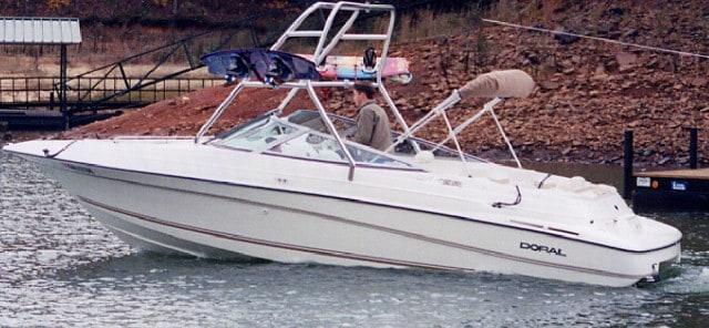 Doral Bowrider boat on water with Atlantic Towers Air Tower installed and a person seated inside near a rocky shore.