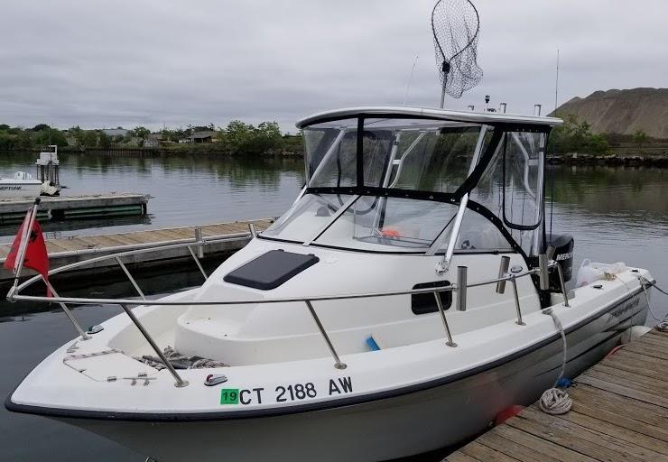 Hydra Sports boat equipped with Atlantic Towers top enclosure docked by a wooden pier in calm water.