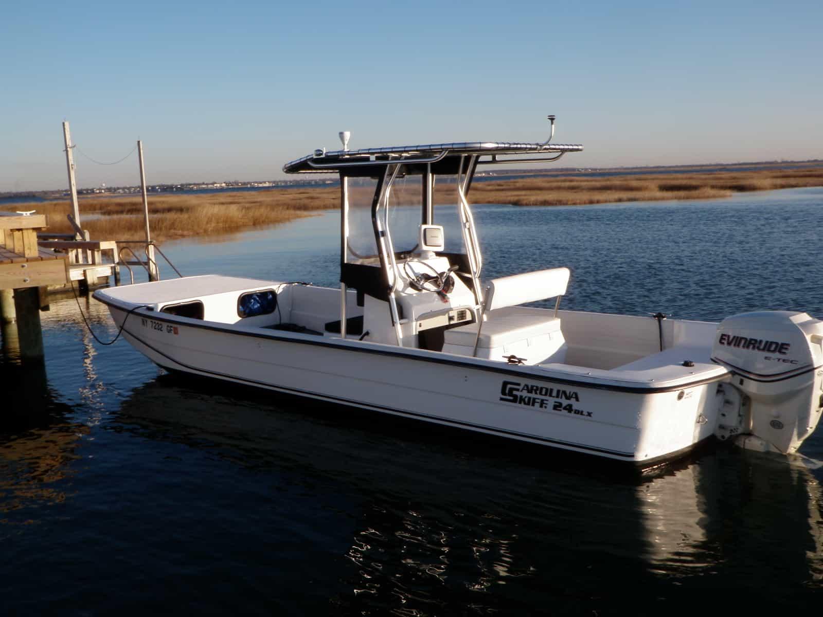 White Carolina Skiff 24 DLX boat with Atlantic Towers T-Top and an Evinrude outboard motor docked on calm water.