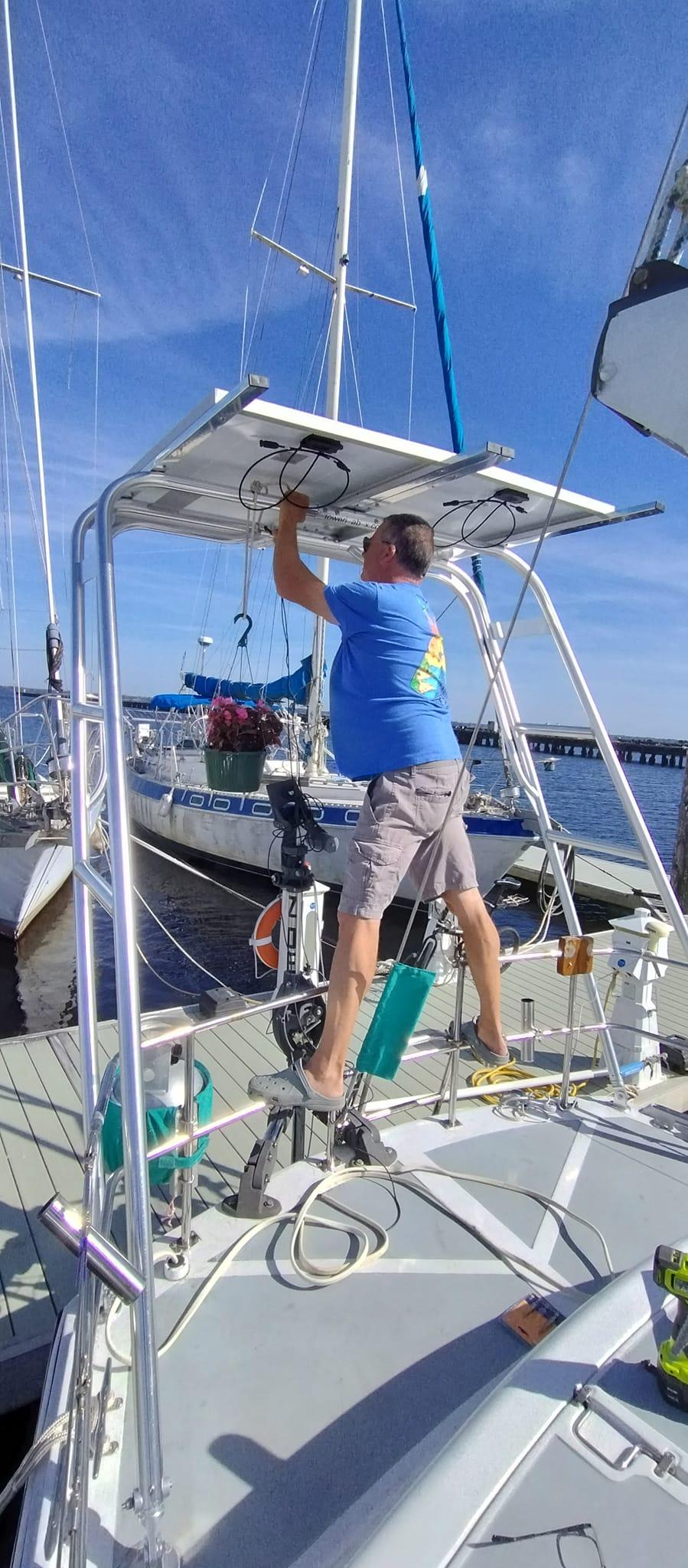 A person adjusts the Atlantic Towers Arch on a boat at the dock, with various equipment and sailboats in the background.