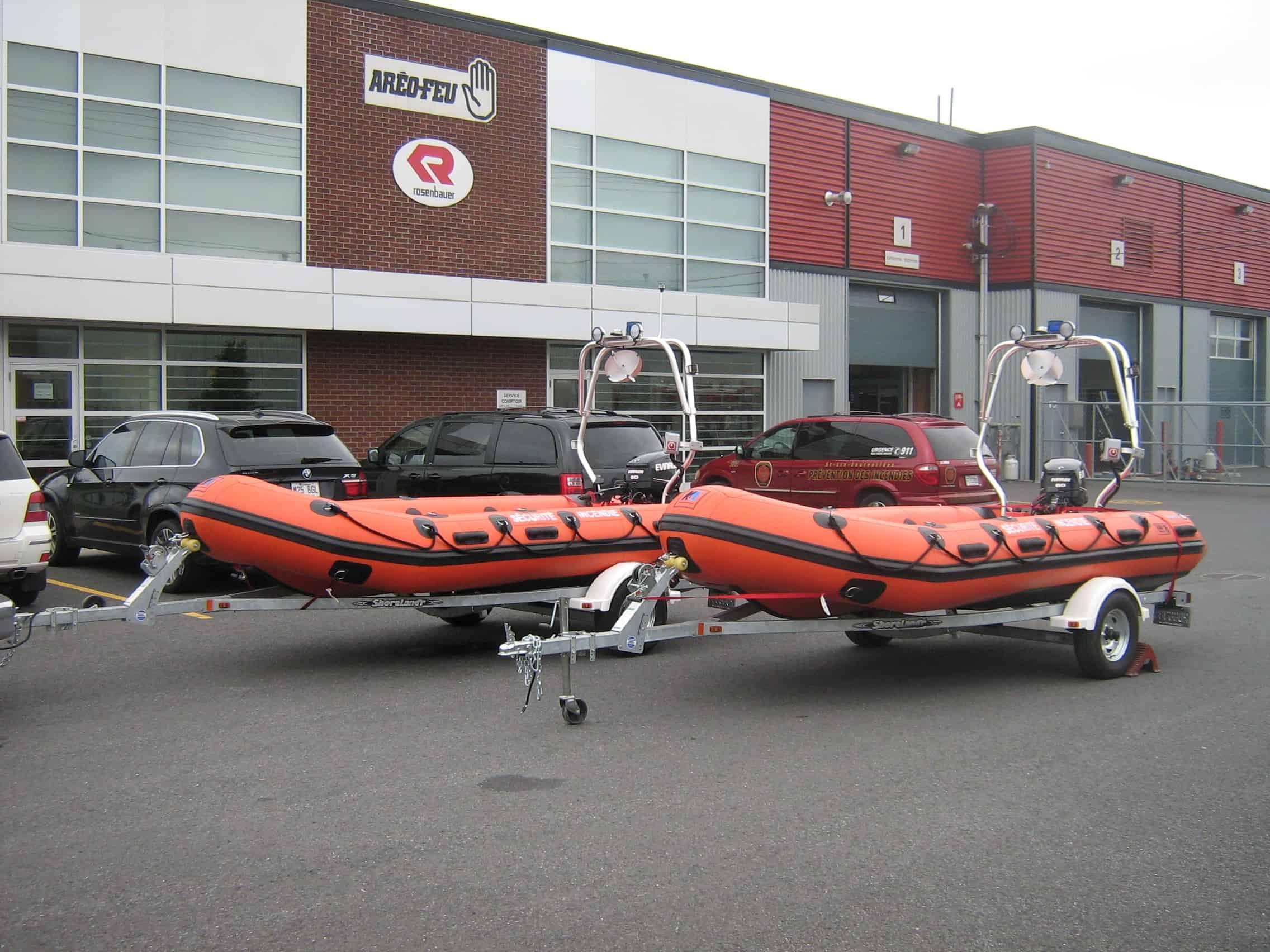 Two orange rigid inflatable boats equipped with Atlantic Towers Arches on trailers parked outside a commercial building.