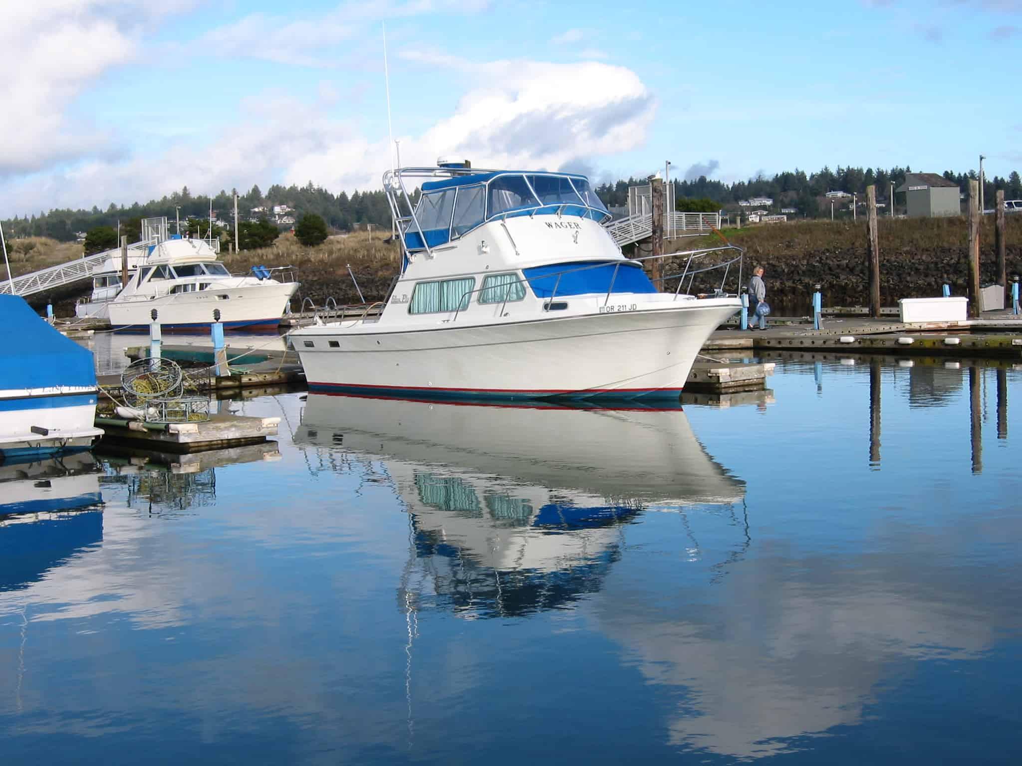 Glass Ply 28 boat with Atlantic Towers arch, white hull with blue canvas, docked at marina with calm water reflection.